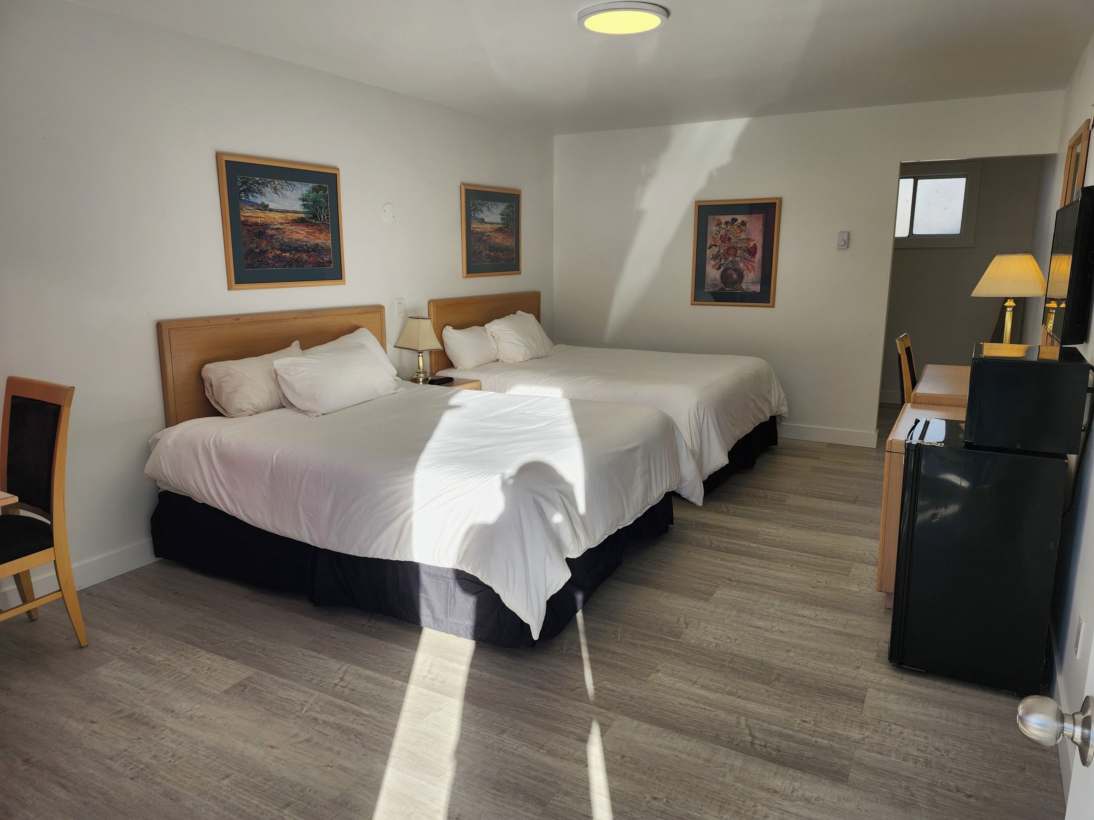 Una habitación de hotel con dos camas, un escritorio, una silla y un refrigerador.
