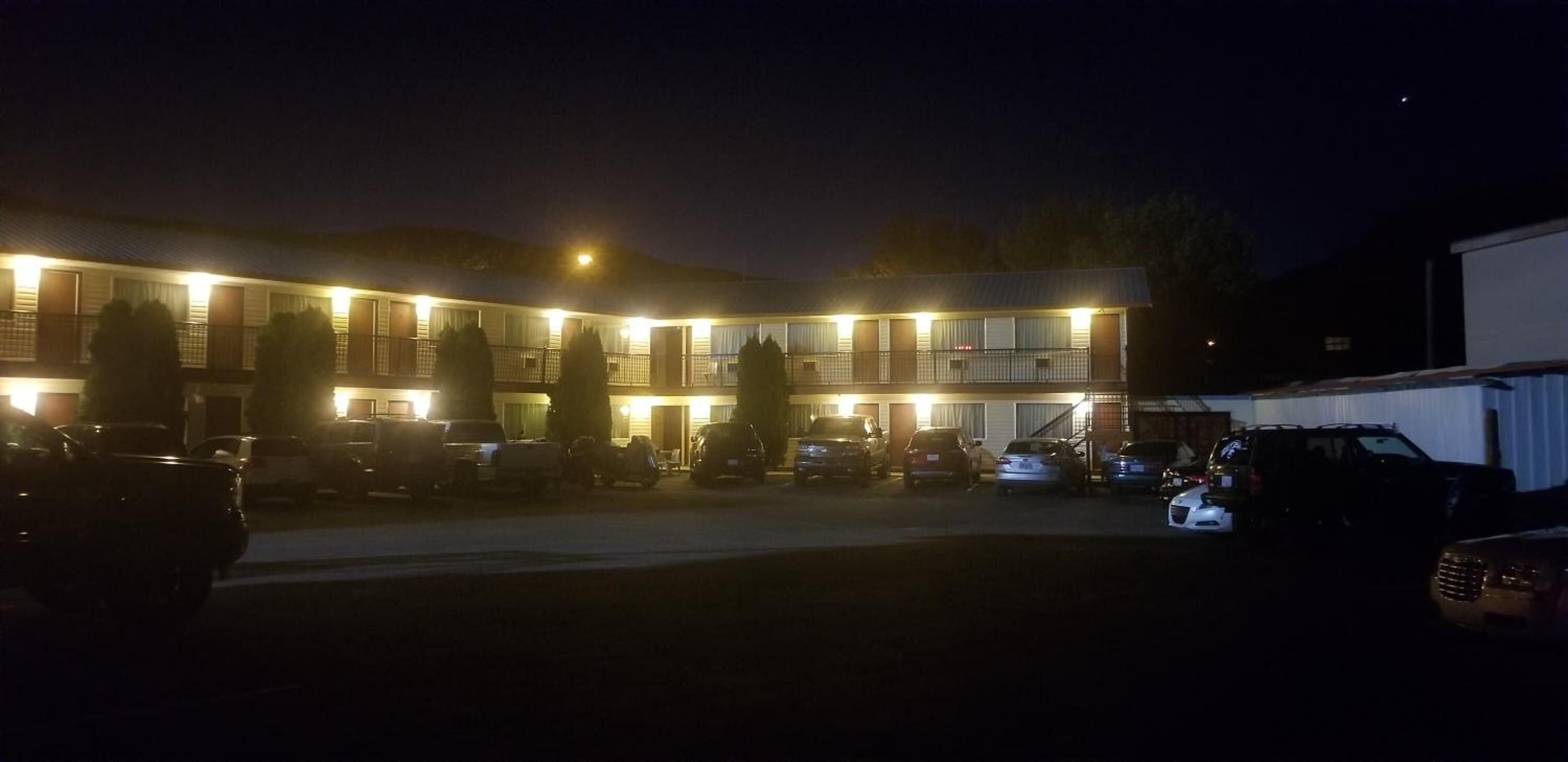 Un motel con varias habitaciones, un estacionamiento y un pequeño edificio adyacente a la estructura principal.