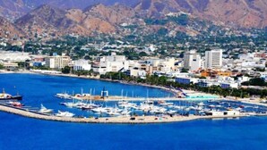 A coastal marina with boats docked, surrounded by residential buildings and mountains in the background. - La Villana Hostel (Santa Marta)