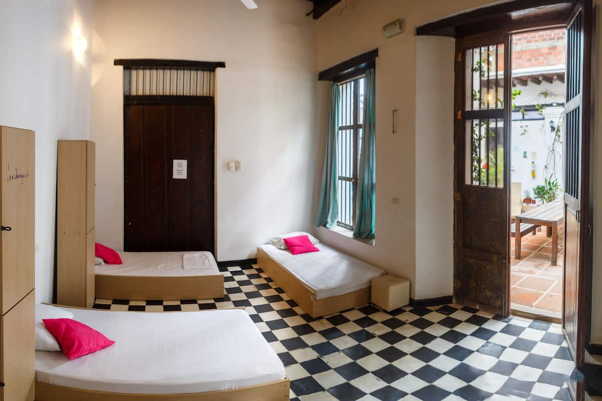 A room with two single beds, a wooden wardrobe, a checkered floor, and a window with curtains.