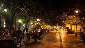 An outdoor dining area with tables and chairs under a tree canopy, surrounded by buildings with warm lighting. - La Villana Hostel (Santa Marta)