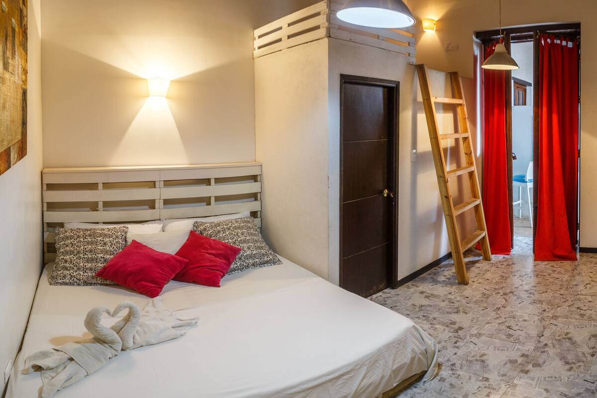 A bedroom with a bed, a wardrobe, a ladder, and a red curtain.
