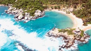 A coastal area with clear turquoise waters, rocky outcrops, and dense tropical vegetation. - La Villana Hostel (Santa Marta)