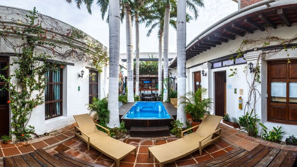 A courtyard with a hot tub, lounge chairs, and potted plants. - La Villana Hostel (Santa Marta)