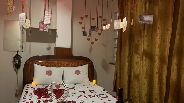 A romantic room with a bed adorned with rose petals and a heart-shaped arrangement, candles, and a bottle of wine on a table. - Hostal Ventura Isabel (Iquitos)