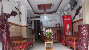 A reception area with a wooden bench, a small table with a vase of flowers, and a Coca-Cola refrigerator. The wall has a sign reading "HOSTAL Ventura Isabel". - Hostal Ventura Isabel (Iquitos)