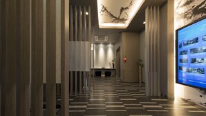 Un pasillo de hotel con una mesa de recepción, una pantalla digital y un piso estampado.
