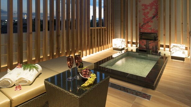 Un moderno espacio de spa con un baño de piedras climatizado, asientos tipo lounge y vistas del horizonte urbano al anochecer.