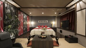 Una habitación de hotel moderna con una cama grande, un televisor de pantalla plana, una mesa de centro y una zona de estar con sofá y sillones.