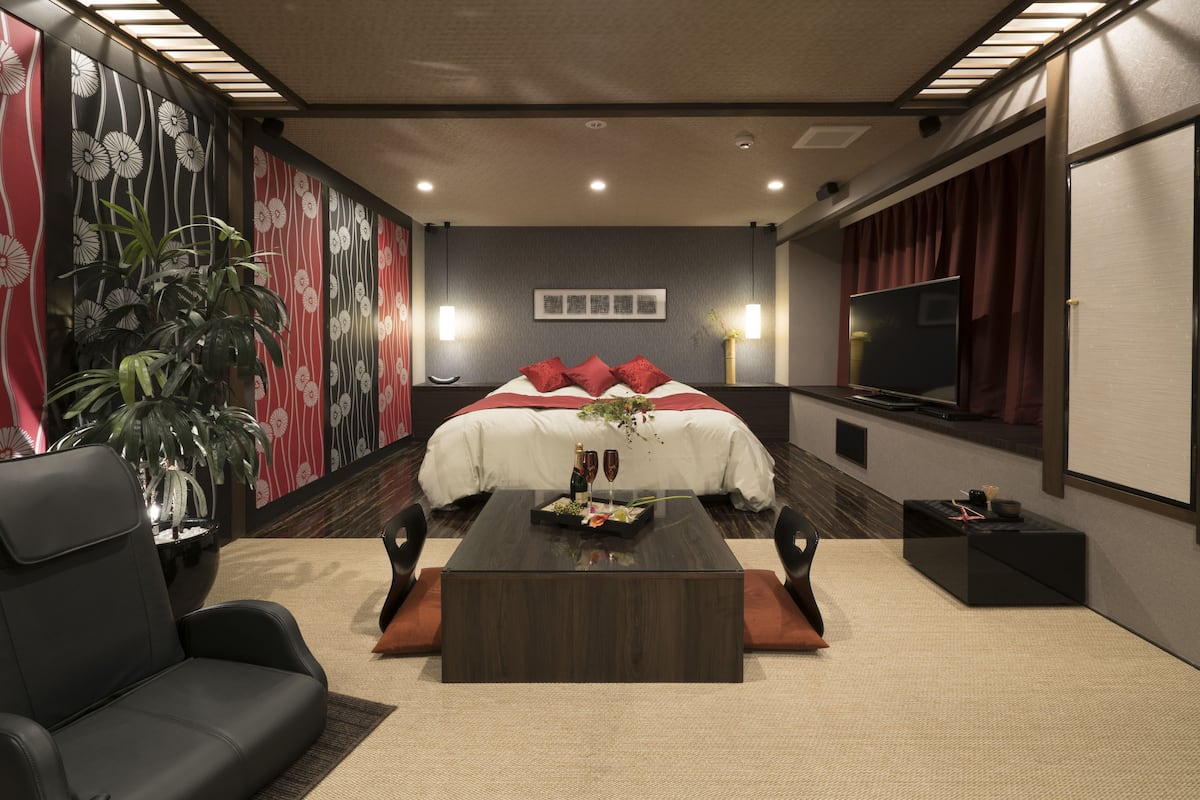 Una habitación de hotel moderna con una cama grande, un televisor de pantalla plana, una mesa de centro y una zona de estar con sofá y sillones.