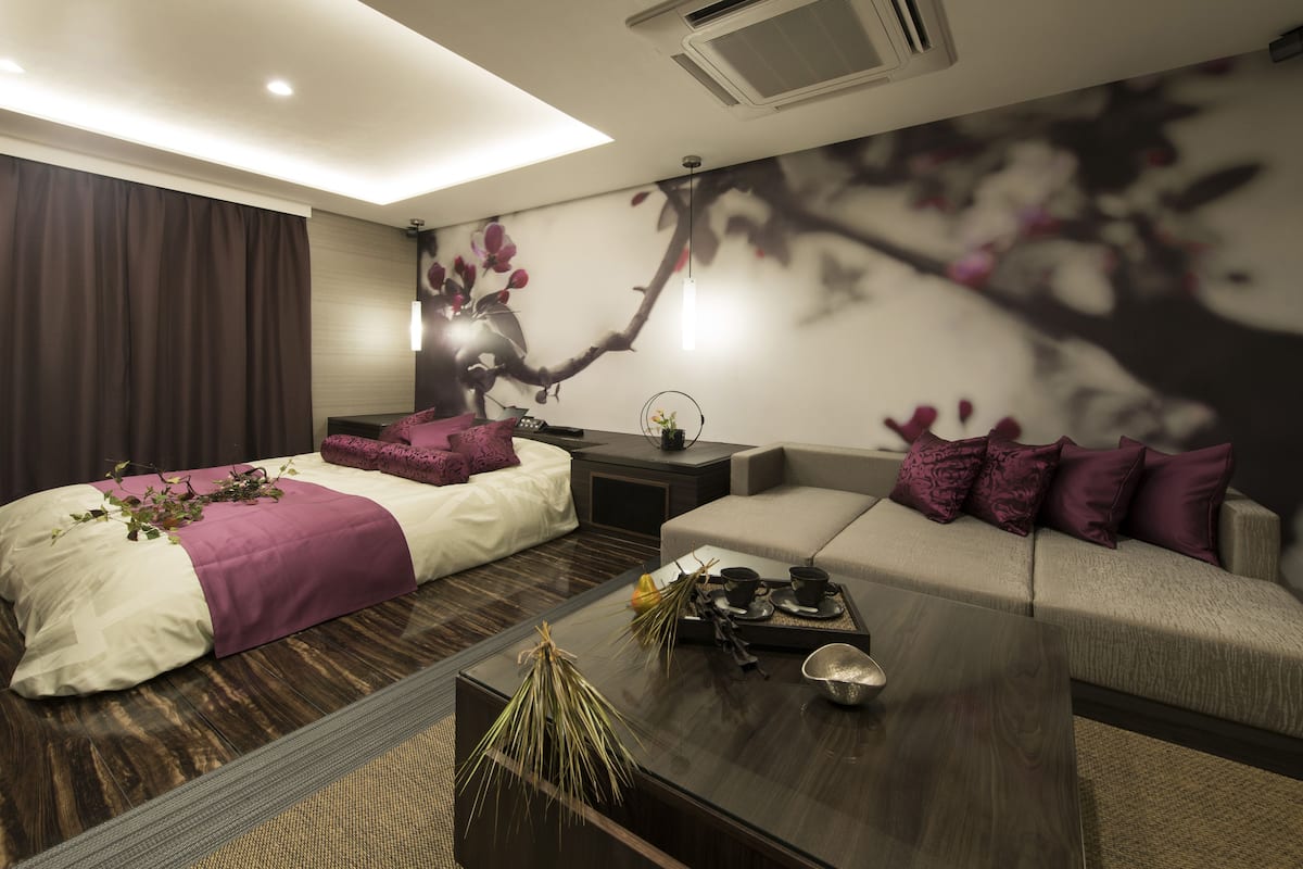 Una habitación de hotel moderna con una cama, un sofá, una mesita de centro y un mural en la pared.