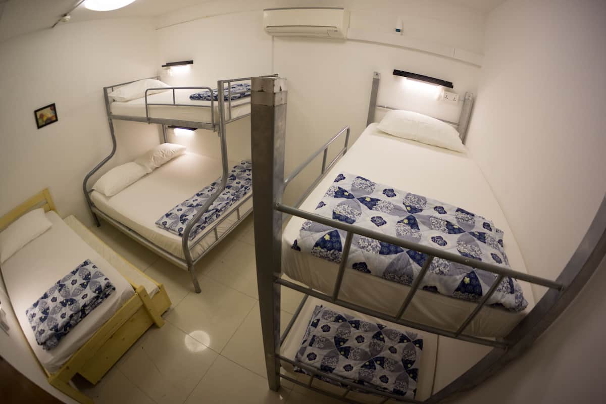 A dormitory room with bunk beds, a single bed, and a ceiling fan.