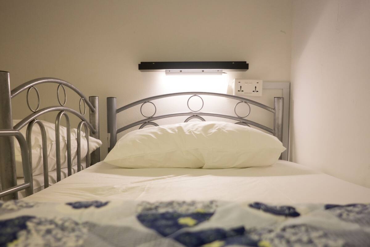 A single bed with a metal frame, a white pillow, and a patterned bedspread.