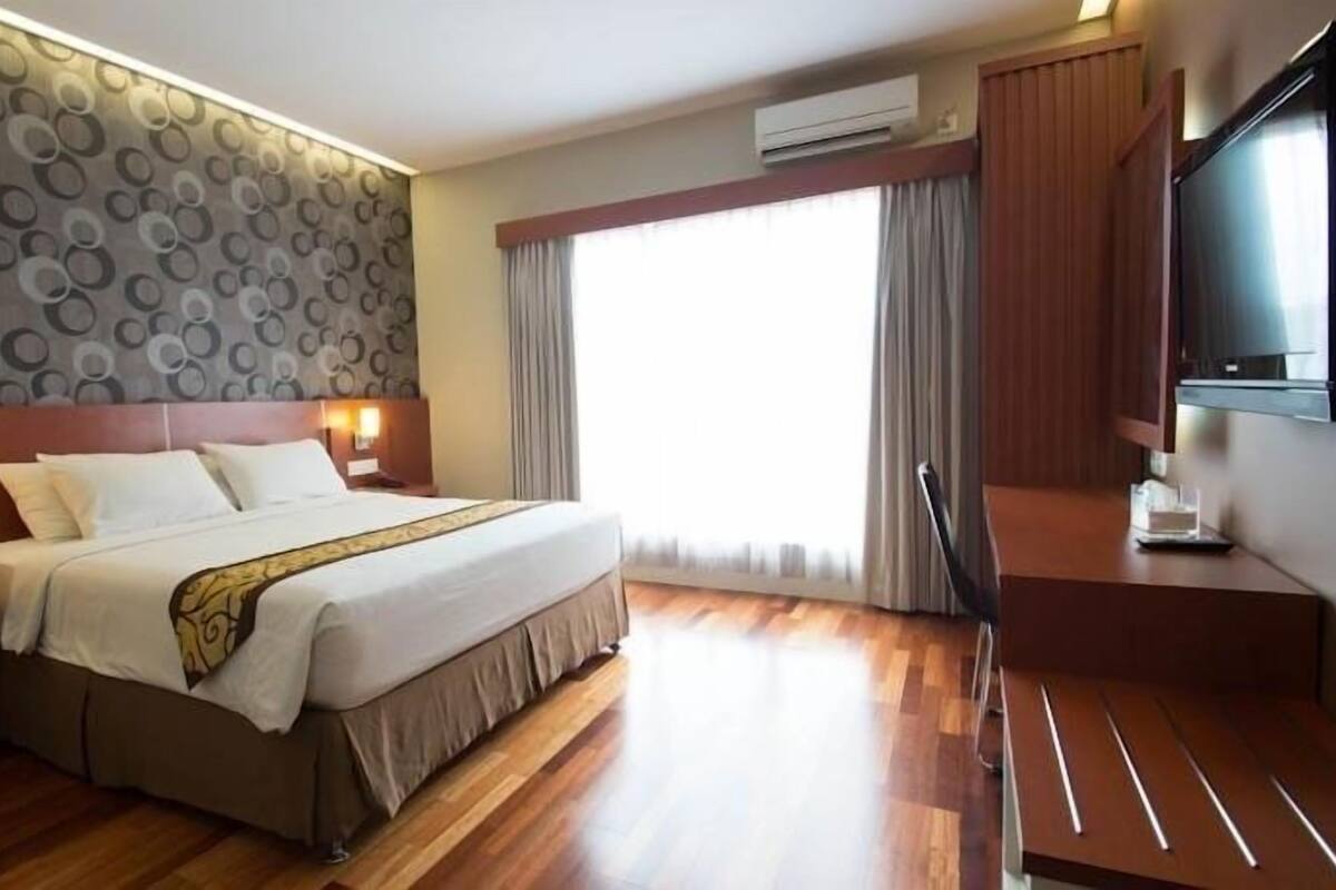 A hotel room with a large bed, a TV, a desk, and a window with curtains.