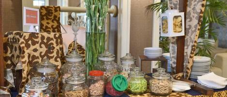 A buffet setup with patterned tablecloths, glass jars of food, and a decorative centerpiece.