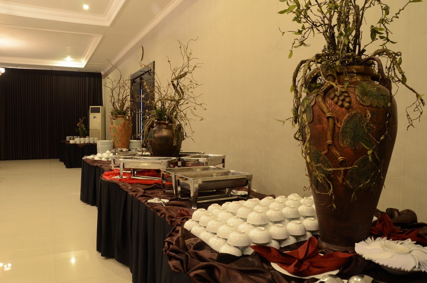 A buffet setup with multiple serving stations, a large decorative vase, and a black curtain backdrop.