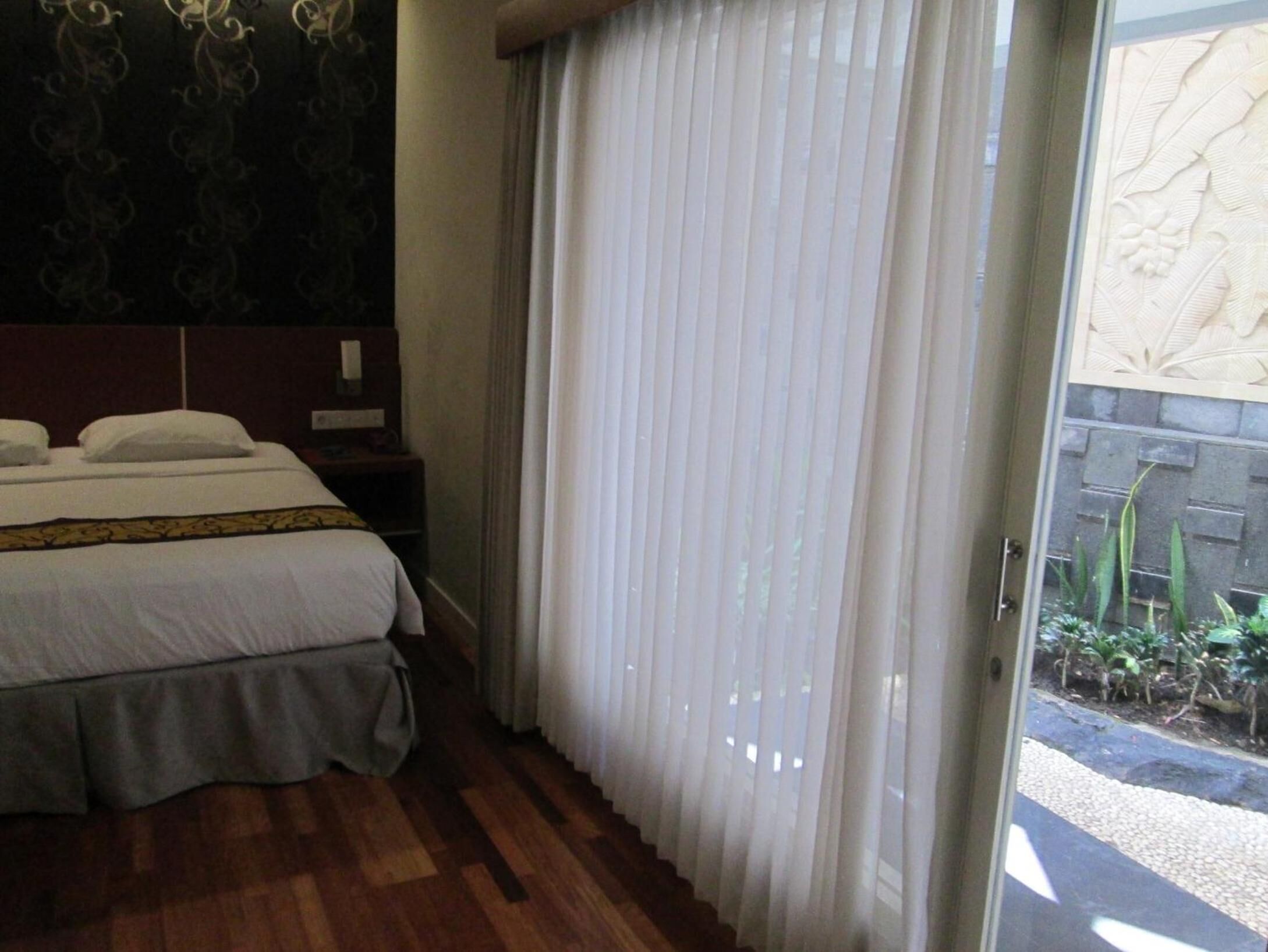A hotel room with a bed, a nightstand, and a window with sheer curtains.