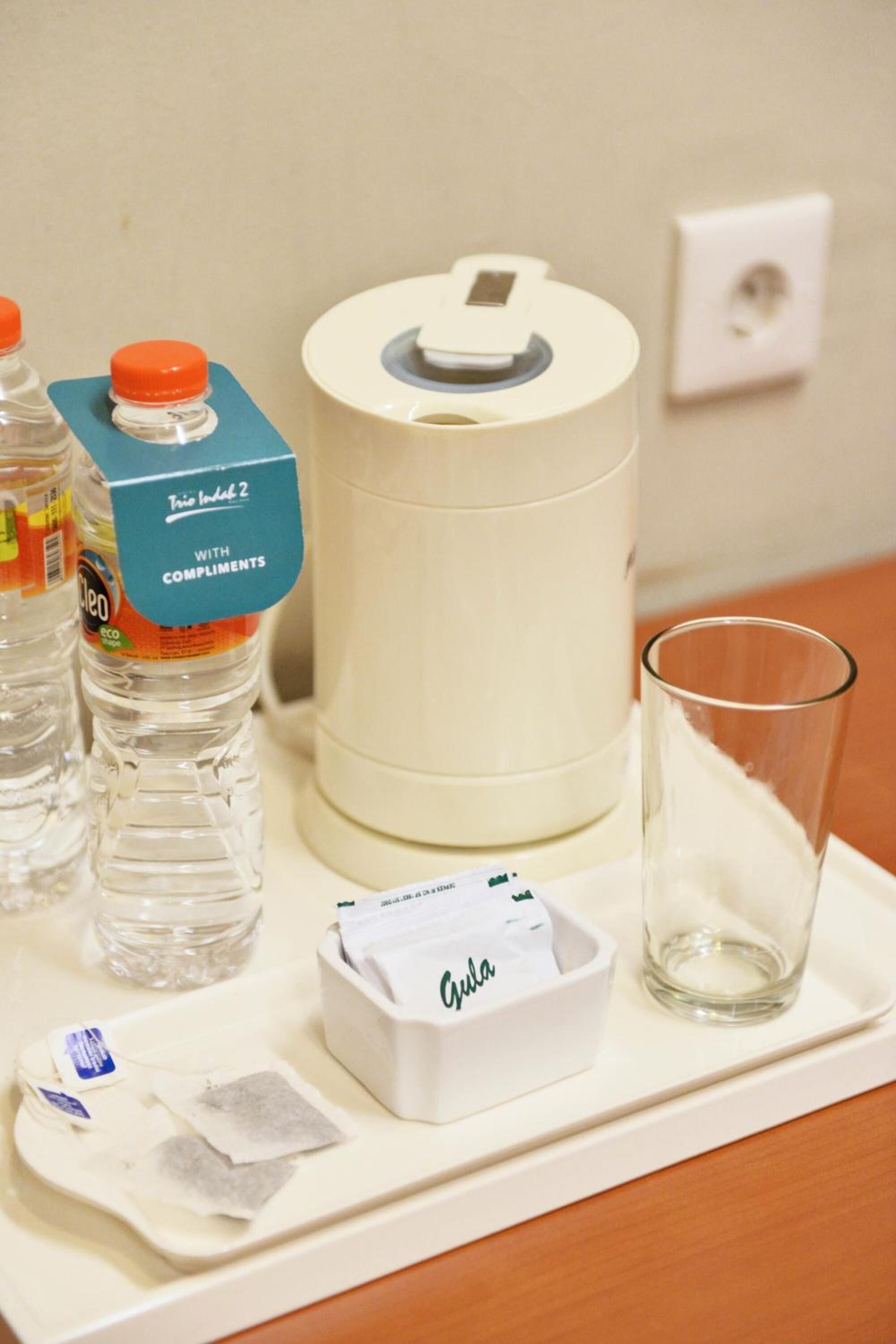 A hotel room tray with a bottle of water, a glass, a tissue box, and a roll of toilet paper.