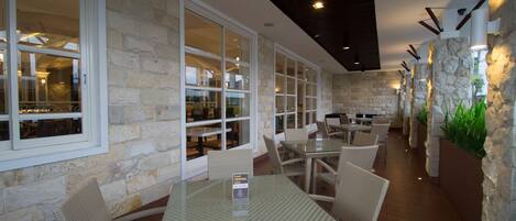 An outdoor dining area with stone walls, glass tables, and wicker chairs.