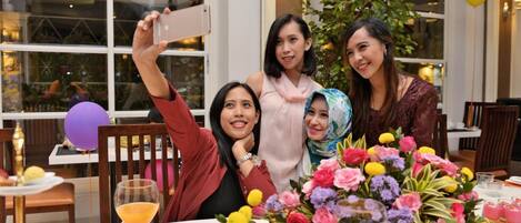 A group of people seated at a table with a floral centerpiece, a glass of orange juice, and a dessert plate.
