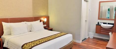 A hotel room with a bed, a nightstand, a bedside lamp, a wooden floor, a bathroom with a sink and mirror.