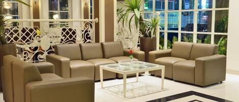 A modern lounge area with beige sofas, a glass coffee table, and potted plants.