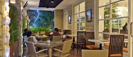 An indoor dining area with wicker furniture, stone walls, and large windows allowing natural light.