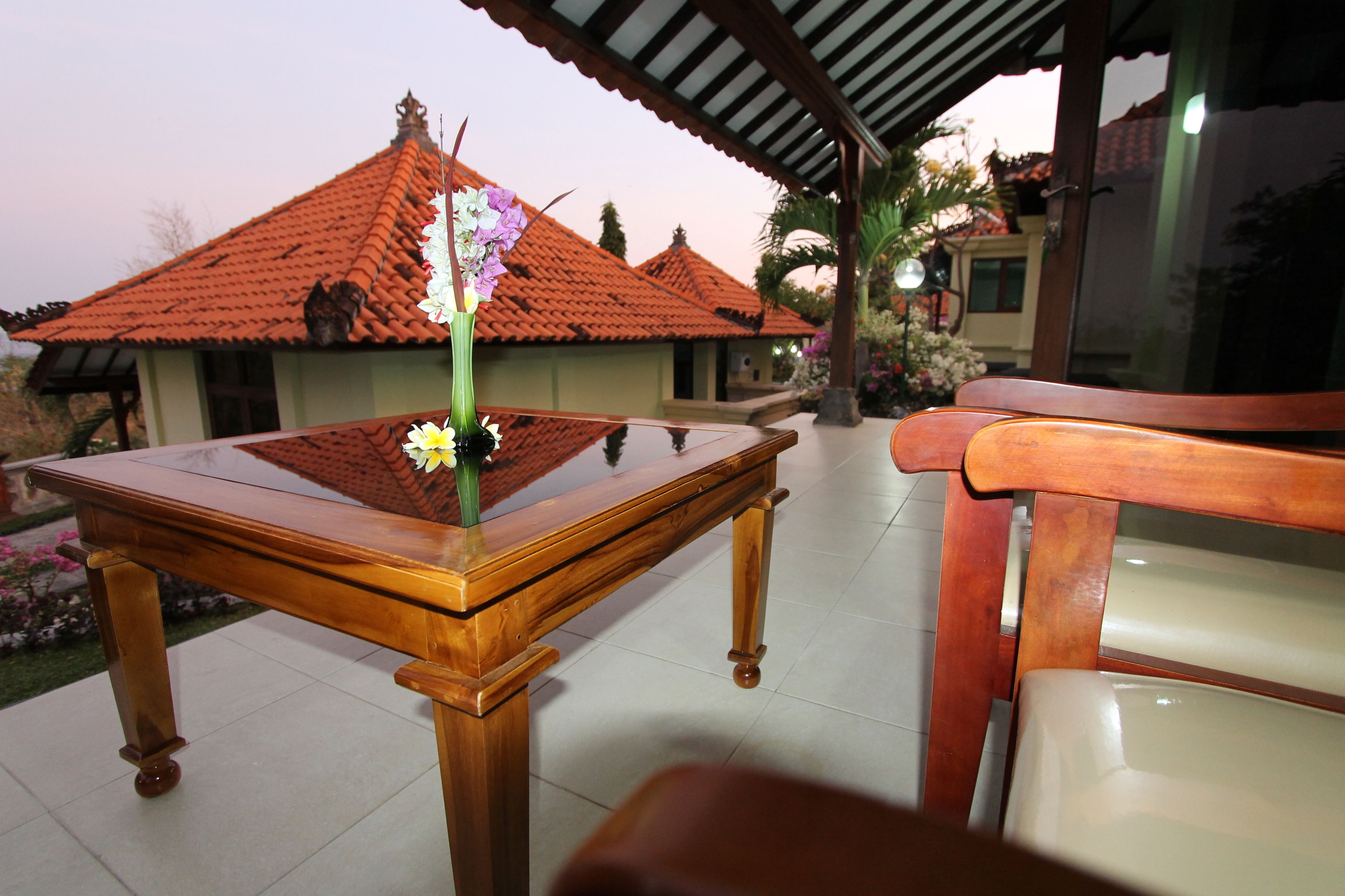 A wooden table with a vase of flowers, a chair, and a view of a building with a tiled roof.