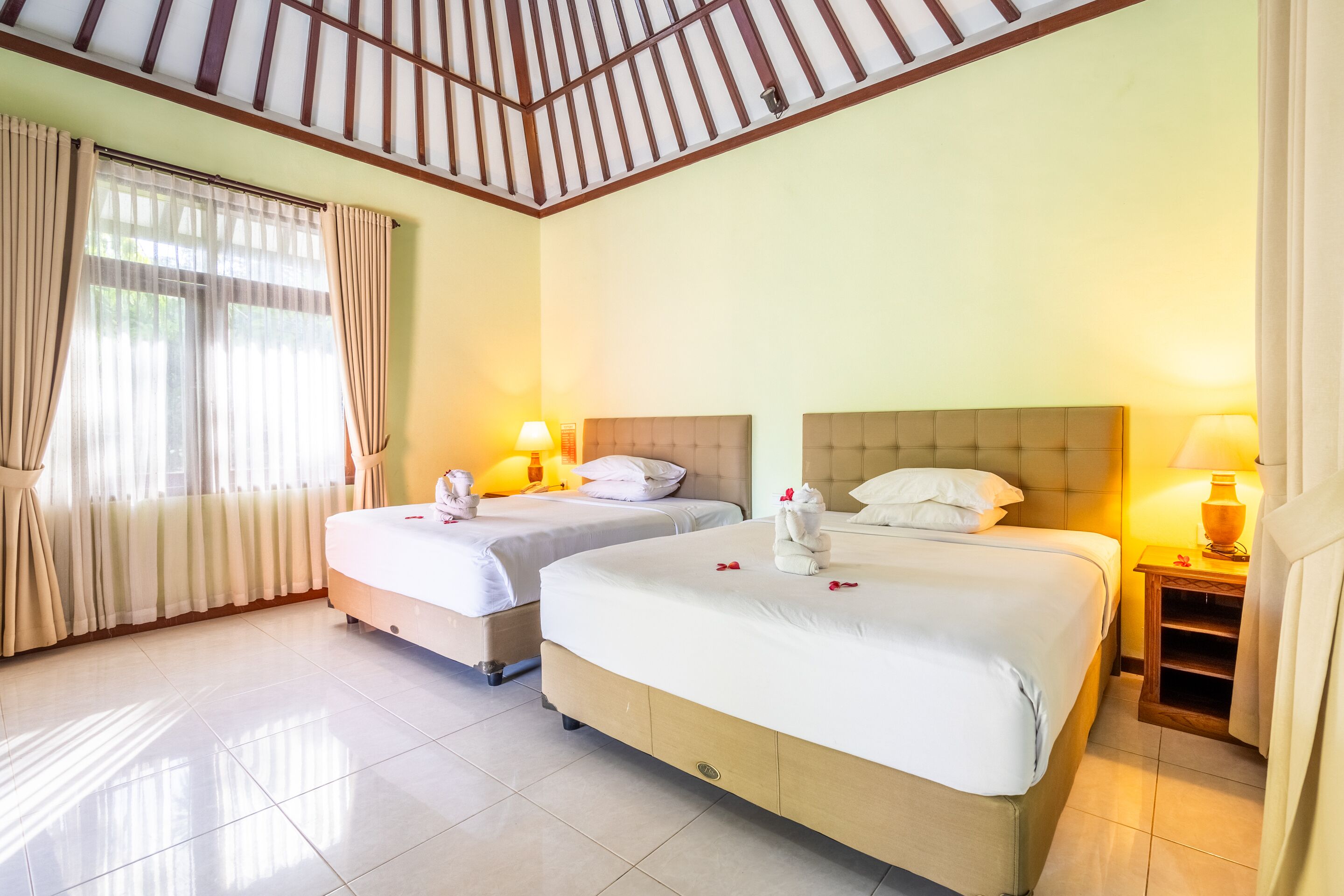 A hotel room with two beds, a wooden ceiling, and a window with curtains.