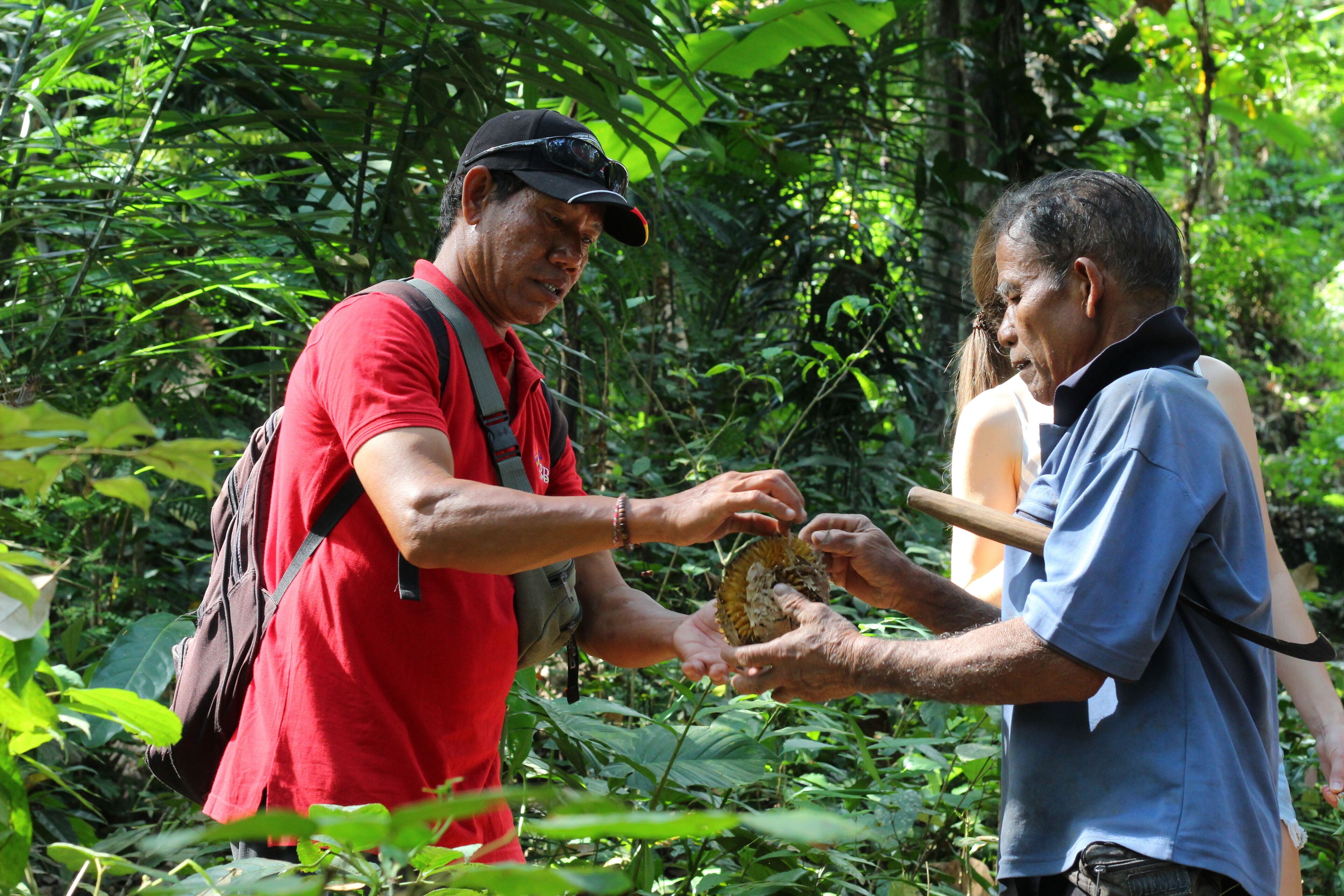 Dos personas intercambiando una concha en un bosque frondoso y verde.