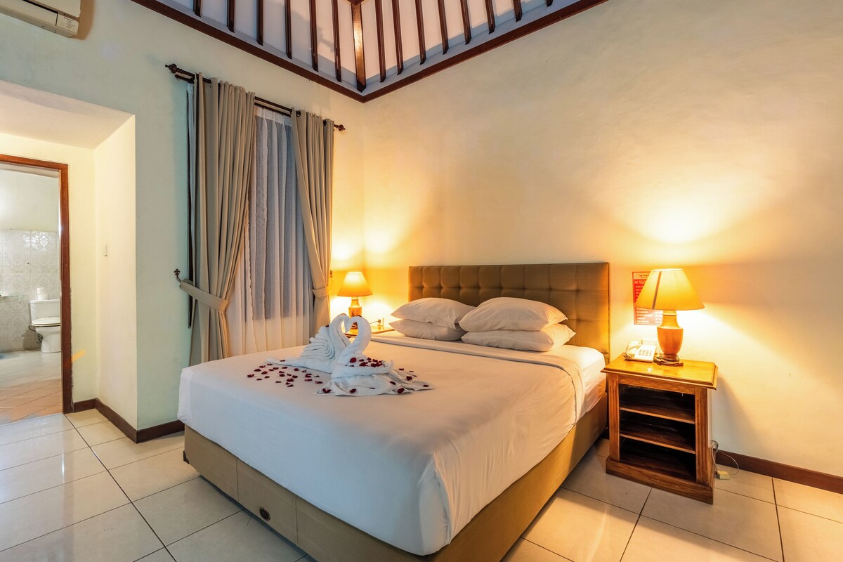 Une chambre d’hôtel avec un grand lit, deux lampes de chevet, une table de nuit en bois et vue sur la salle de bain.