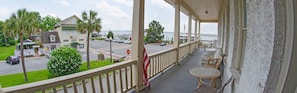A covered porch with outdoor seating, a view of the road, and a building with a flag.