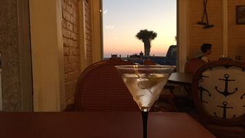 A martini glass on a table with a view of a sunset through a window.