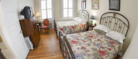 A bedroom with two beds, a wooden dresser, a chair, and a desk with a lamp.