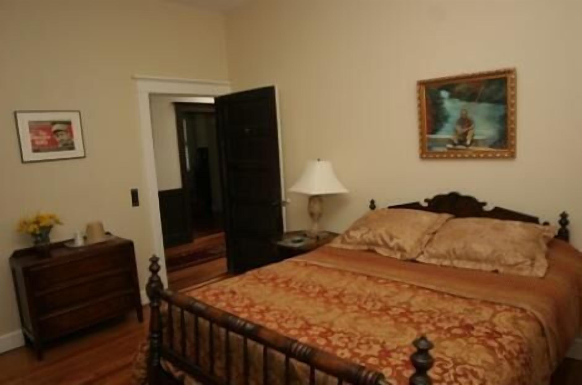 A bedroom with a wooden bed, a nightstand, a lamp, and a painting on the wall.