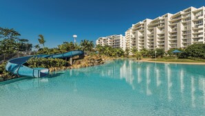 A swimming pool with a water slide, surrounded by palm trees and a multi-story hotel building. - Riviera Mackay (Mackay)