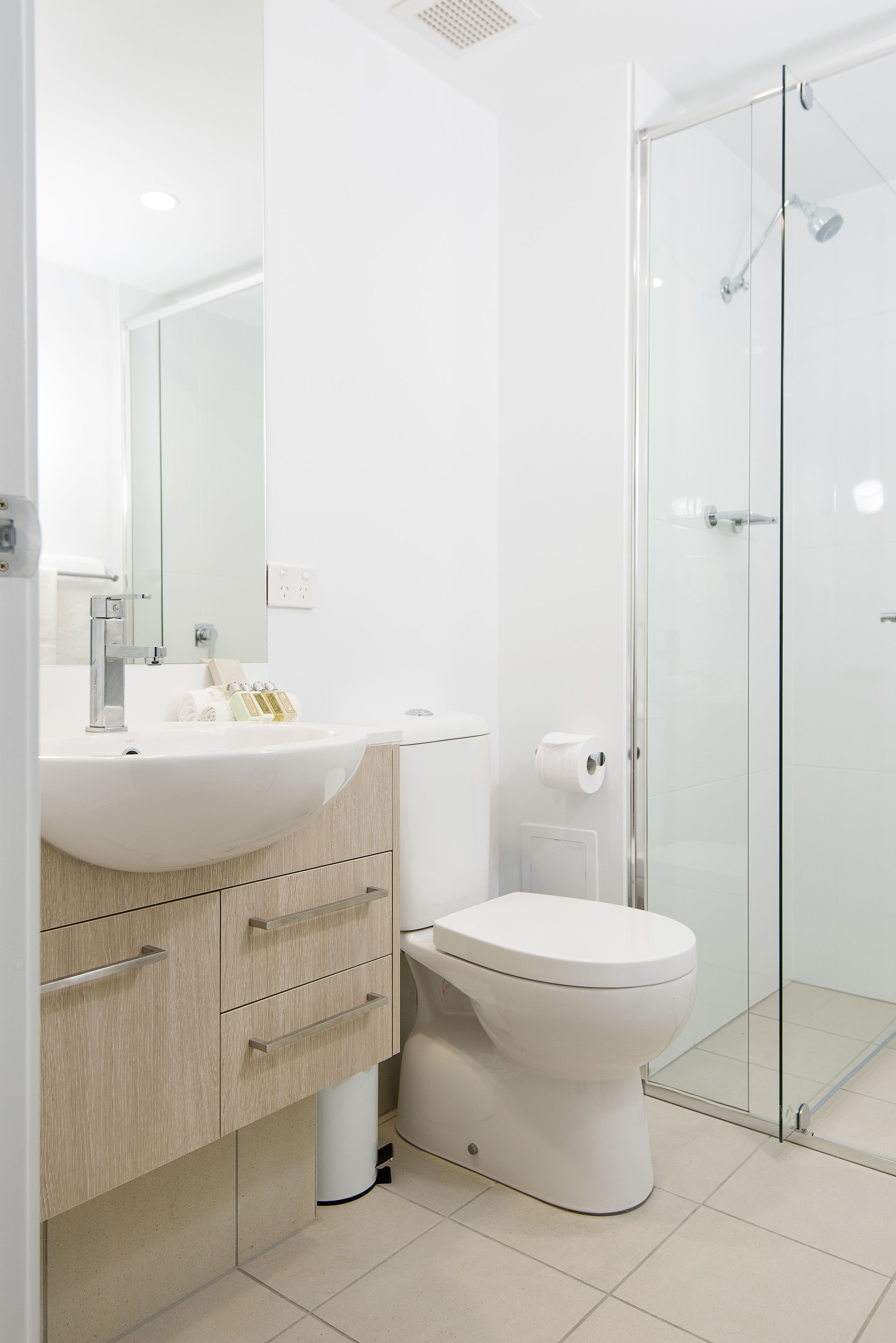 A modern bathroom with a white sink, mirror, and toilet, and a glass-enclosed shower area.