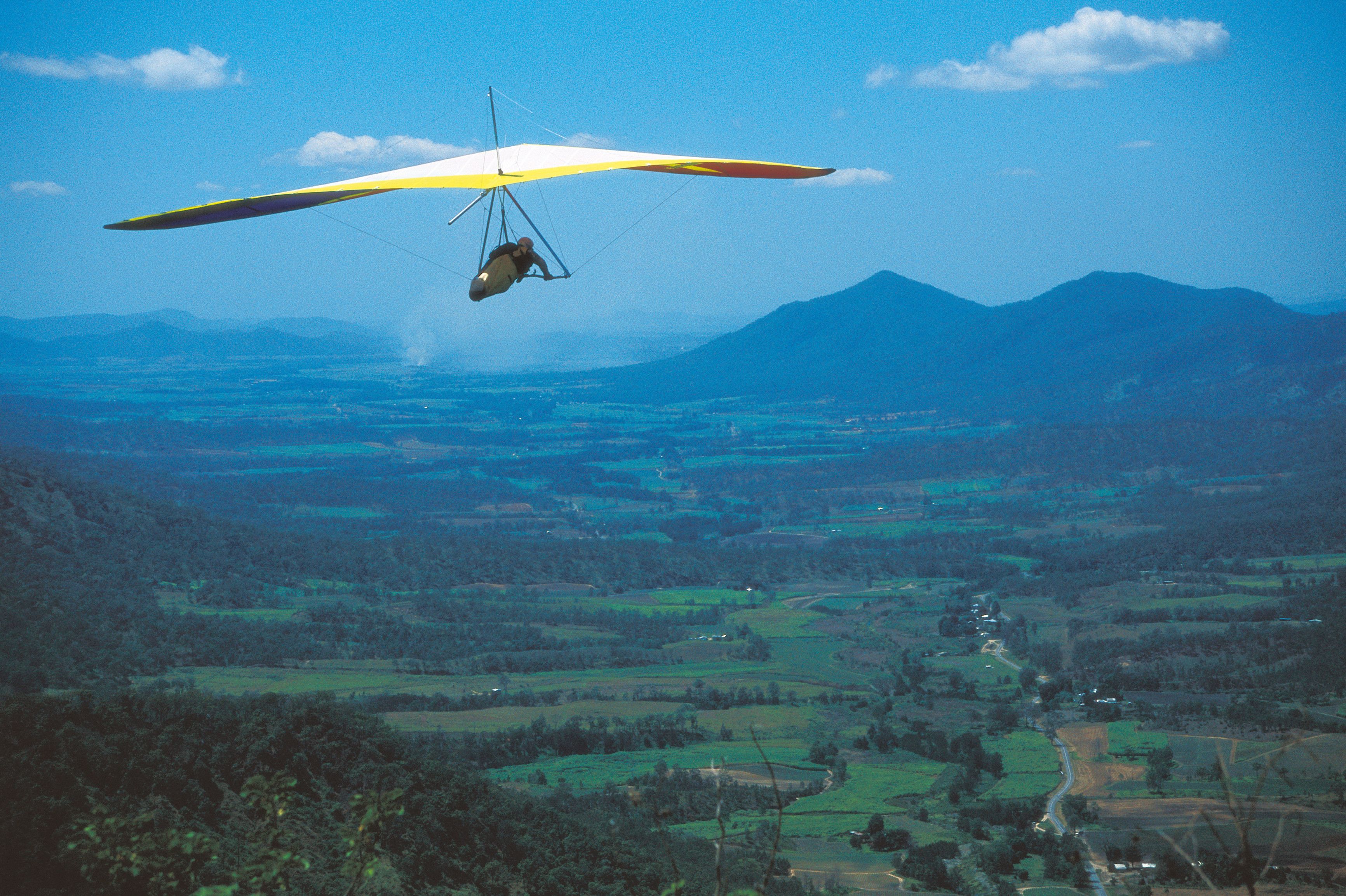 Un planeador vuela sobre un paisaje montañoso con carreteras y vegetación visibles abajo.