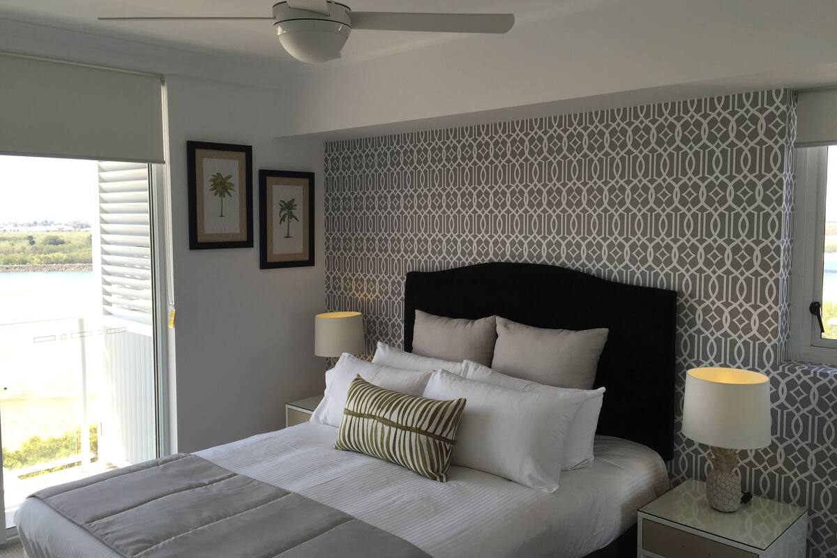 A bedroom with a bed, two bedside lamps, a ceiling fan, and a patterned wall.