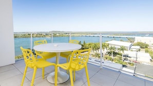 A balcony with a round table and yellow chairs, overlooking a body of water and a bridge. - Riviera Mackay (Mackay)