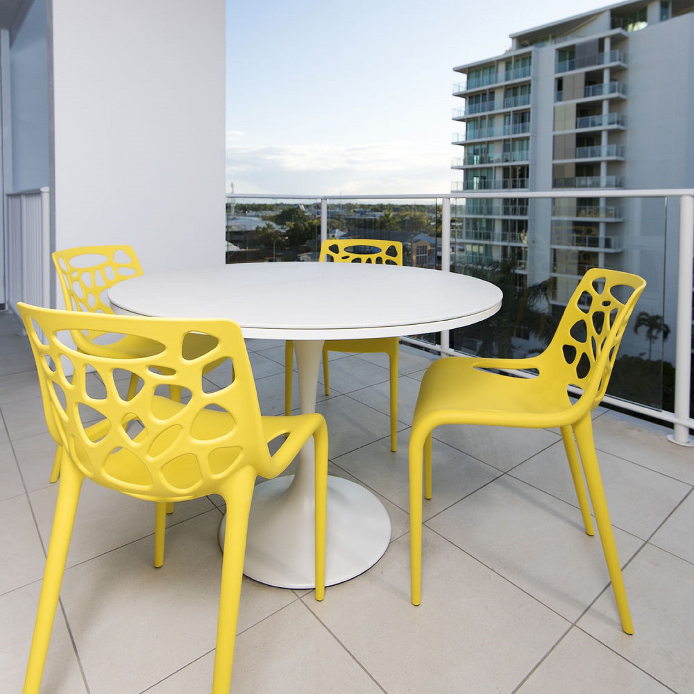 A round table with four yellow chairs on a balcony with a view of a modern building.