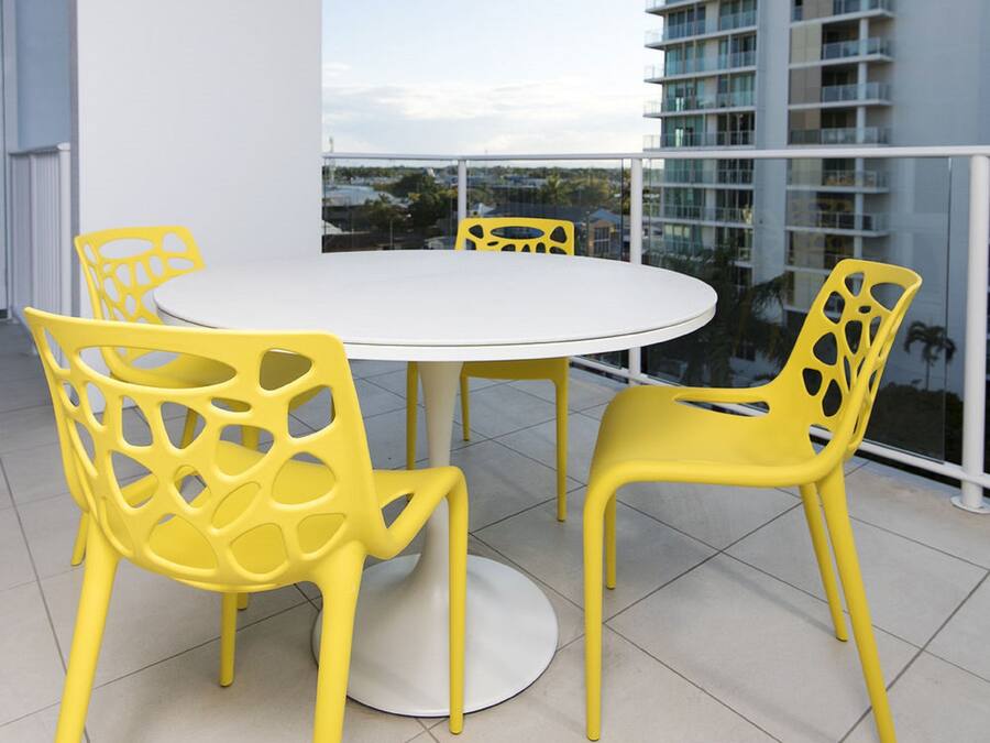 Een ronde tafel met vier gele stoelen op een balkon, met uitzicht op een modern gebouw.