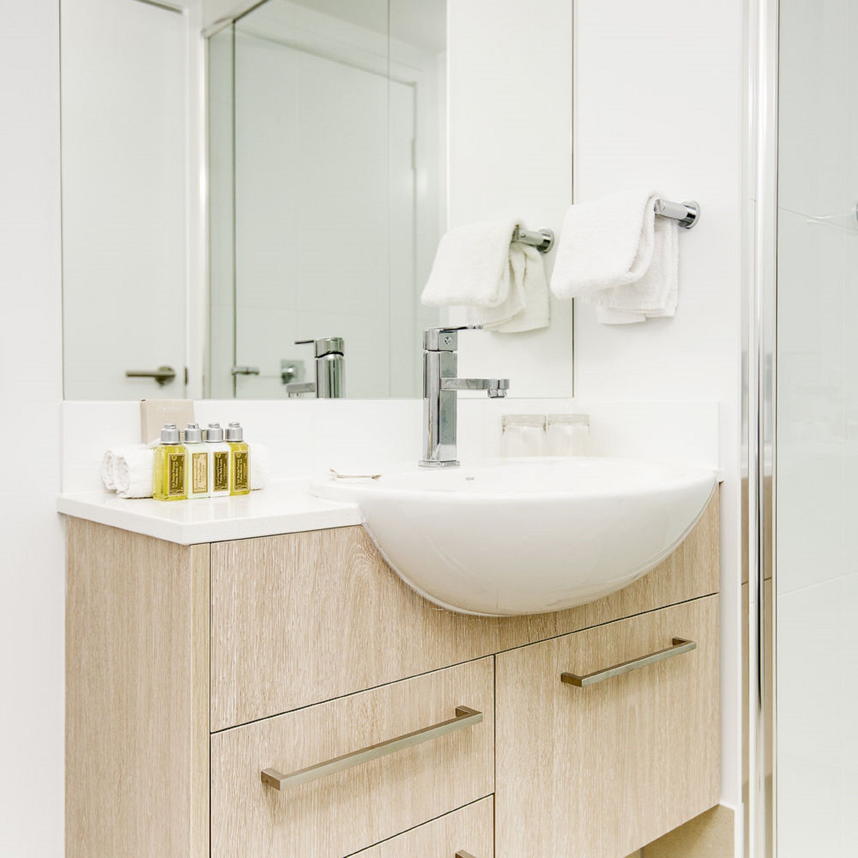 A modern bathroom with a white sink, a large mirror, and wooden cabinetry.