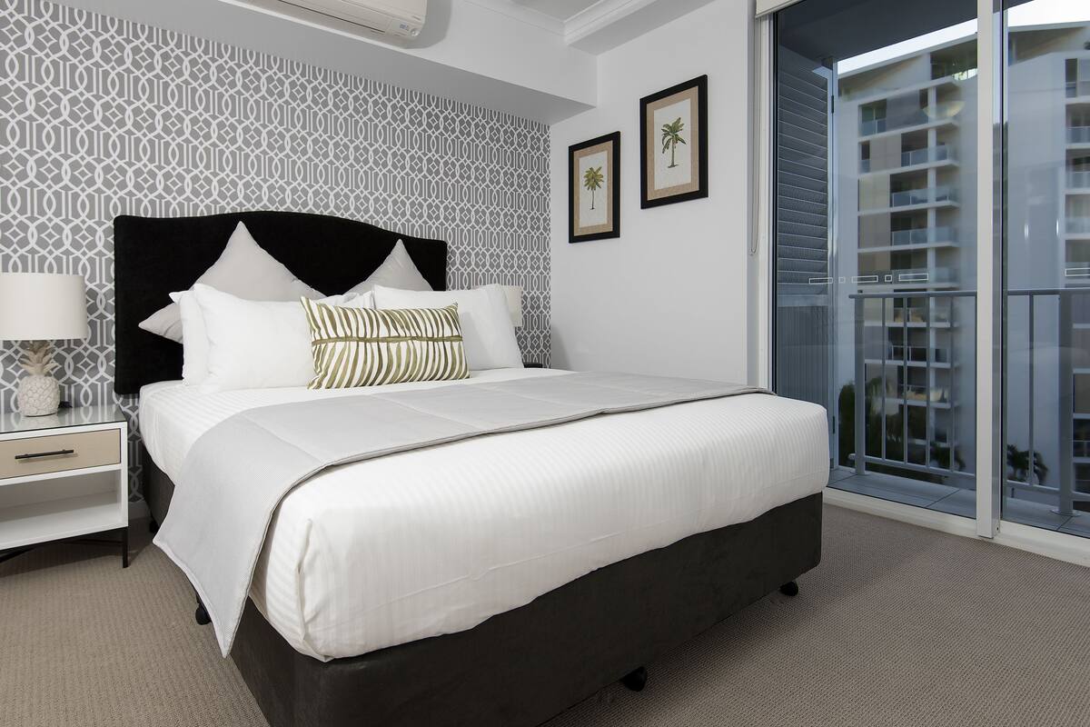 A modern bedroom with a large bed, a nightstand, a lamp, and a patterned wall.