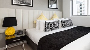 A modern hotel room with a bed, a bedside table with a lamp, and two framed artworks on the wall. - Riviera Mackay (Mackay)