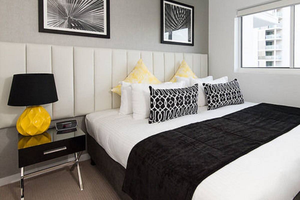 A modern hotel room with a bed, a bedside table with a lamp, and two framed artworks on the wall.