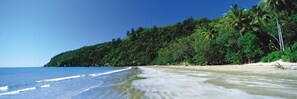 A beach with clear blue water, sandy shore, and dense green foliage. - Riviera Mackay (Mackay)