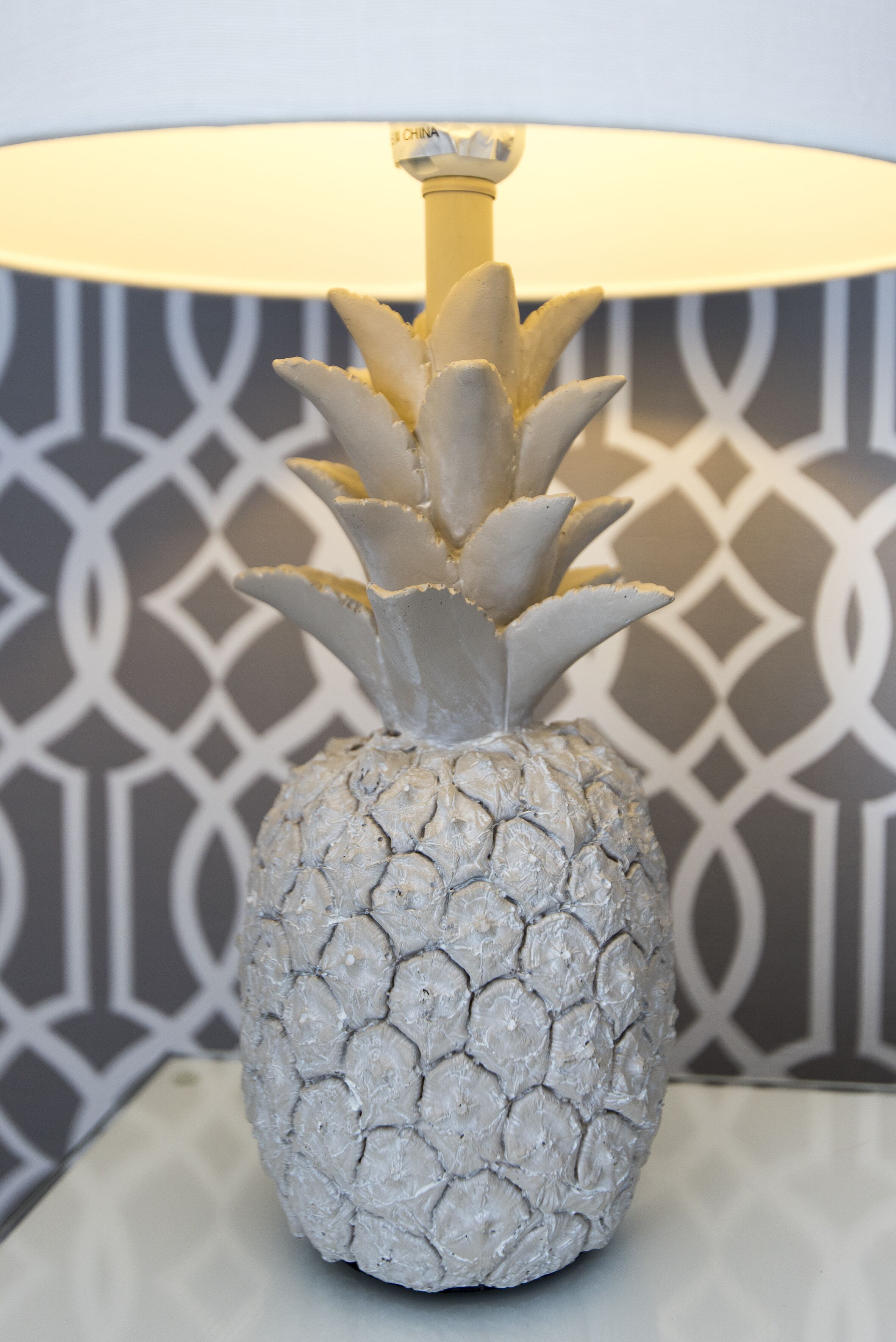 A decorative pineapple lamp with a textured surface and a geometric patterned wall in the background.