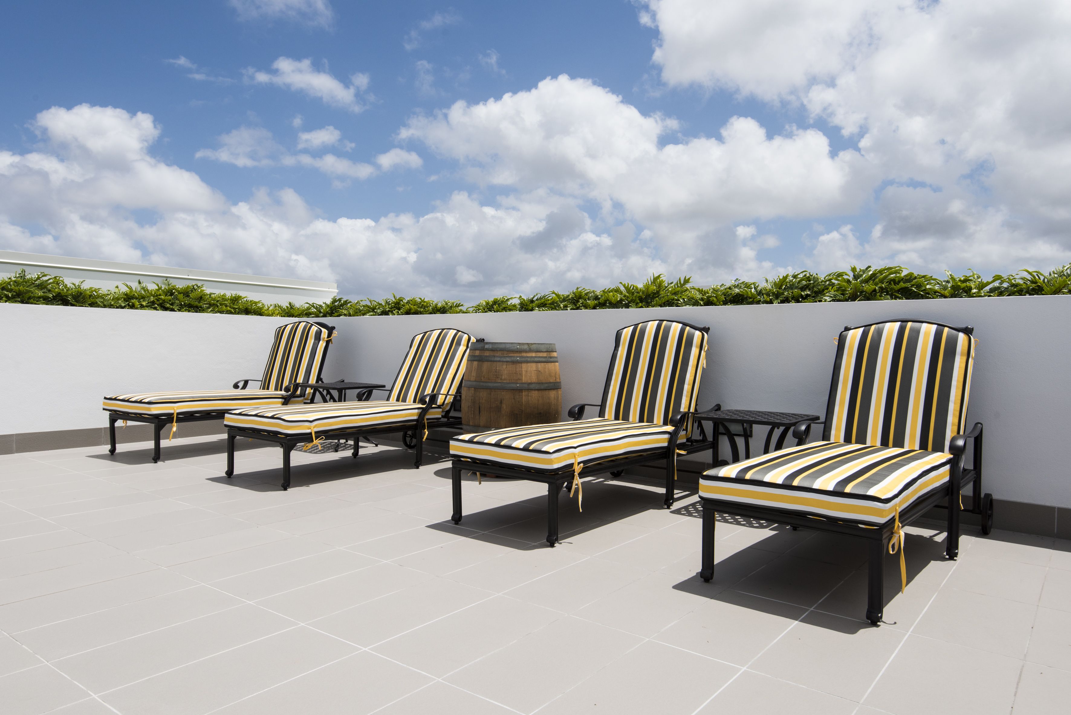 A rooftop terrace with four striped lounge chairs and a small table, surrounded by a low wall and a clear sky.