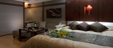 A modern hotel room with a large bed, a sitting area with a table and chairs, and a wall-mounted TV.